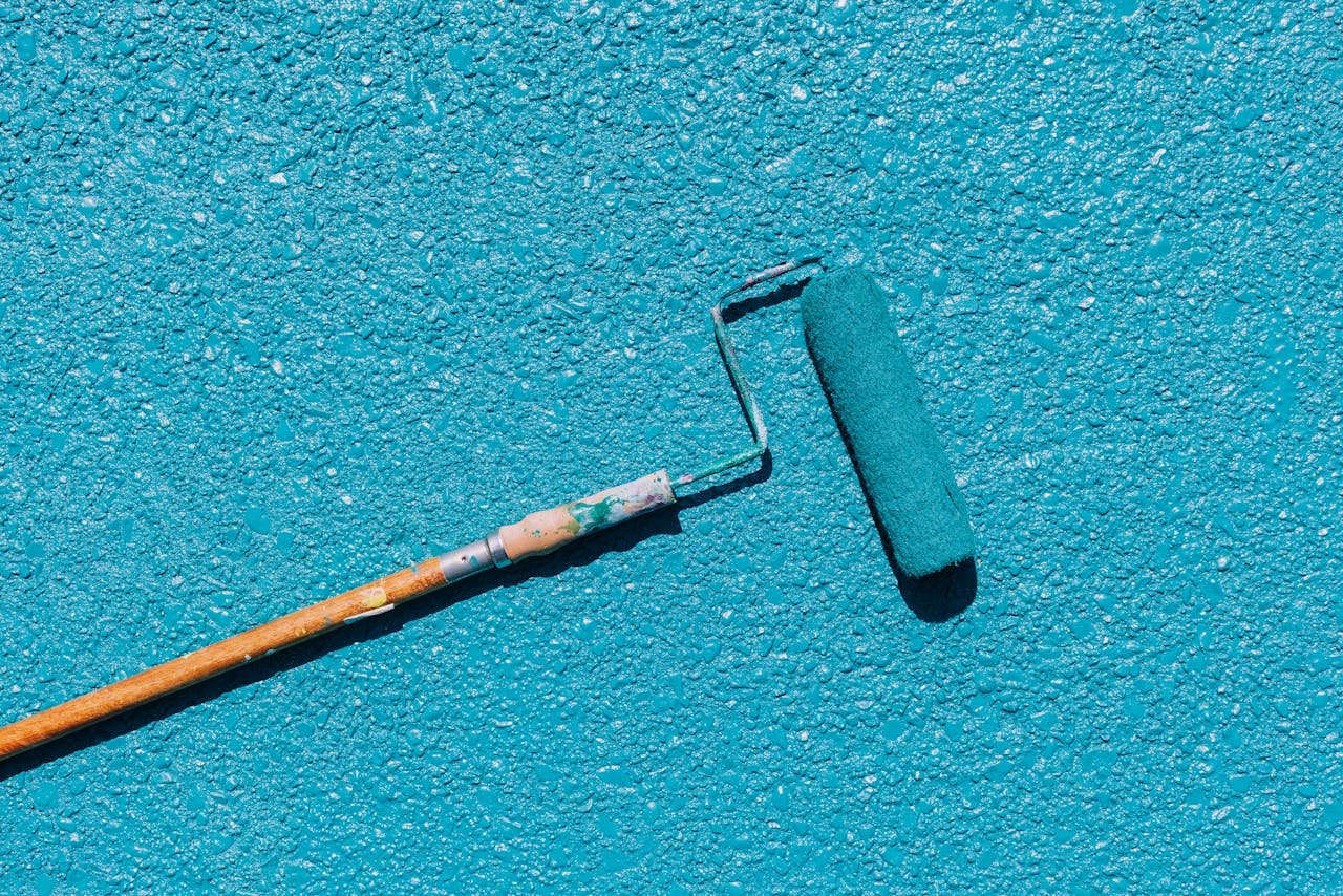 A close-up of a blue paint roller applying paint on a textured wall surface, captured in bright sunlight.
